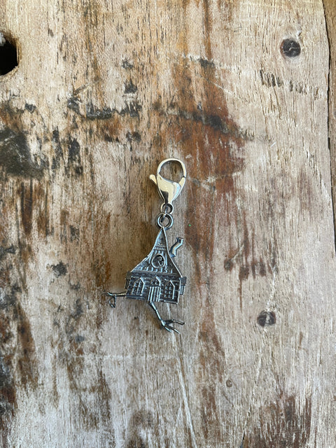 Silver Baba Yaga house shaped charm on a wooden surface