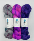 Three skeins of yarn in purple, pink, and gray with labels on a white background