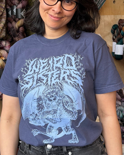 Person wearing a blue t-shirt with a graphic design in front of yarn skeins.
