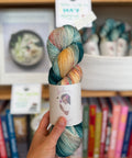 Multicolored skein of yarn held in front of a bookshelf with books and decorative items.