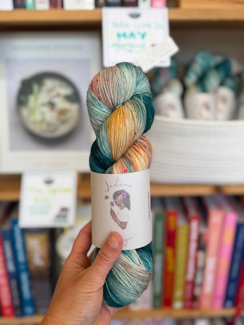 Multicolored skein of yarn held in front of a bookshelf with books and decorative items.