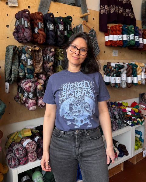 Woman wearing a blue t-shirt with a graphic design in a yarn store.